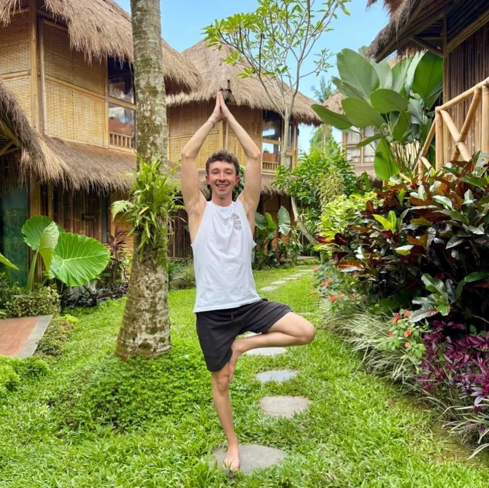 Max holding tree pose on a garden path among tropical plants