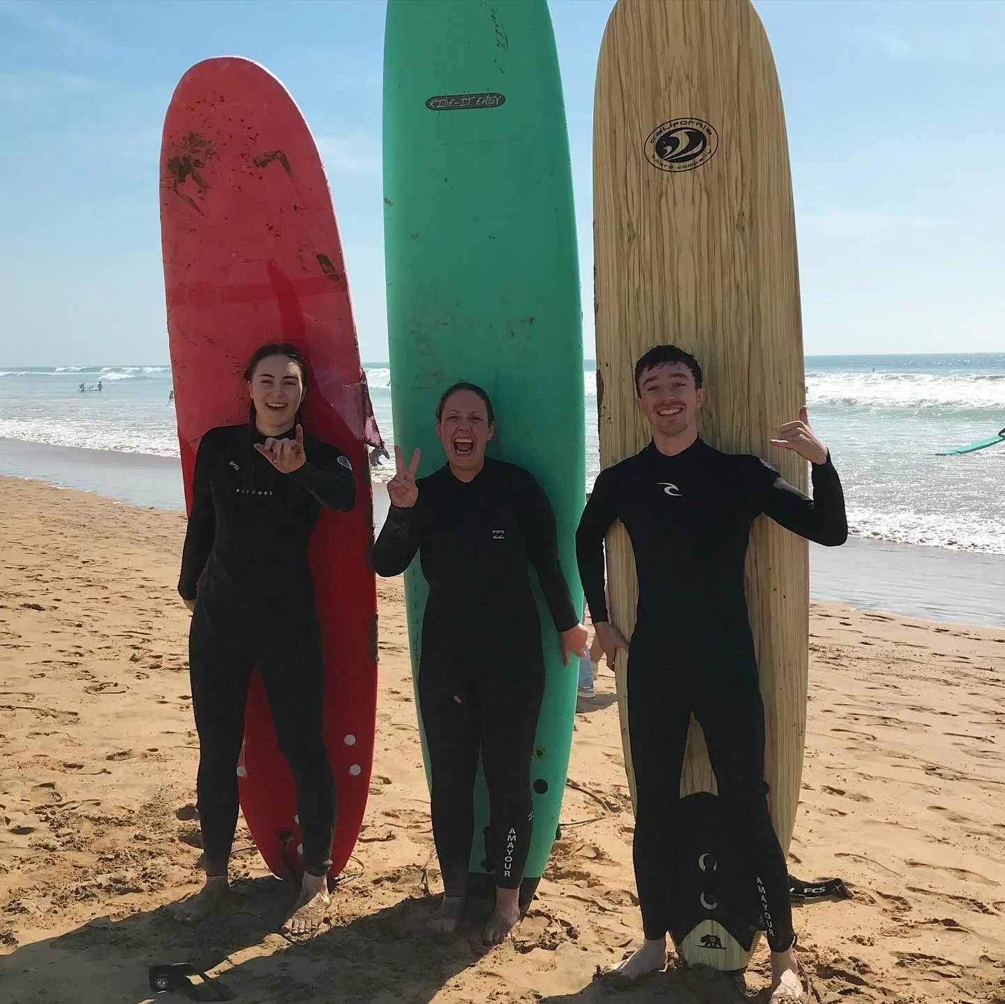 Three friends standing on the beach with colourful surfboards