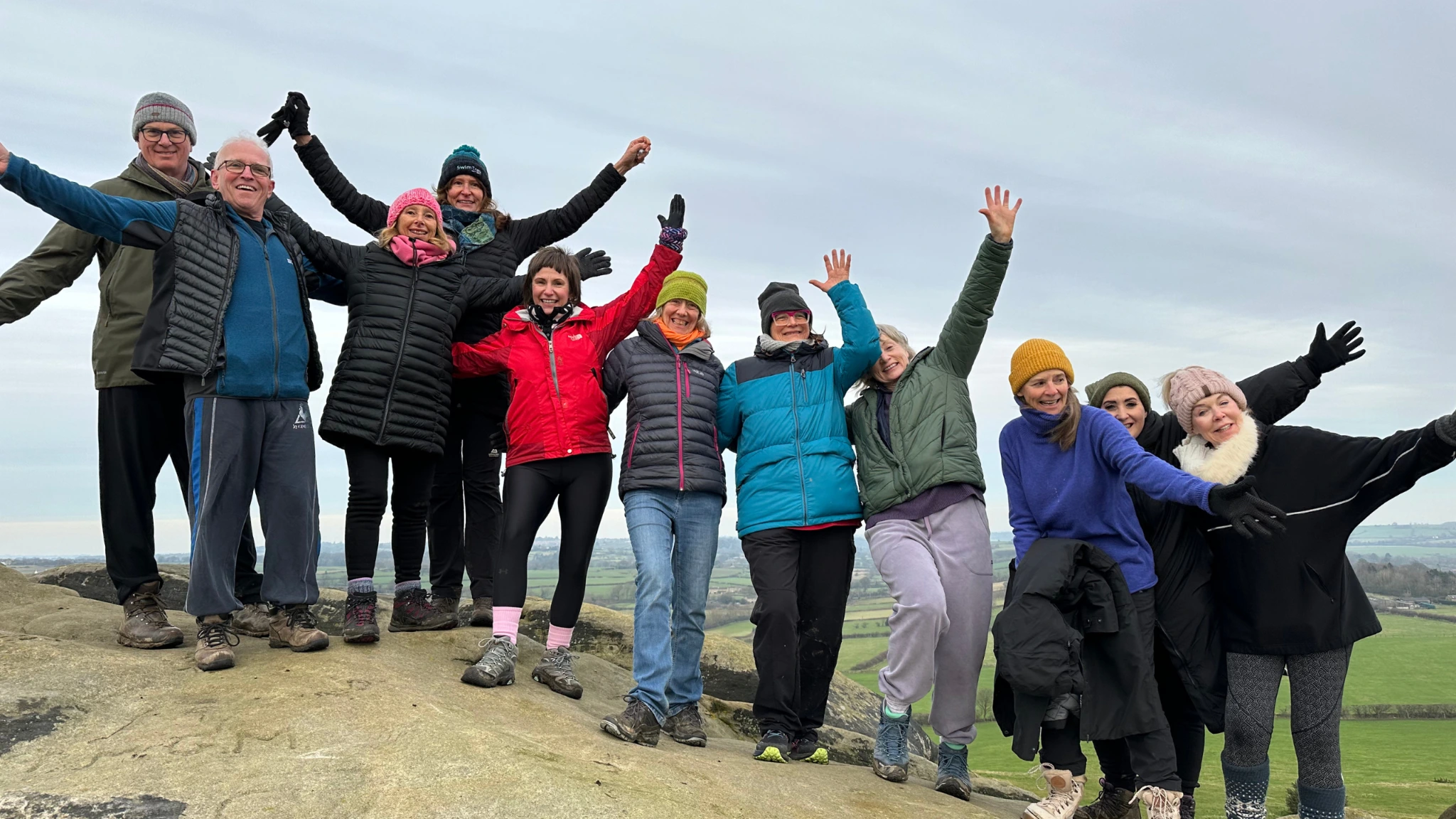 A smiling group with arms outstretched on a rocky coastline